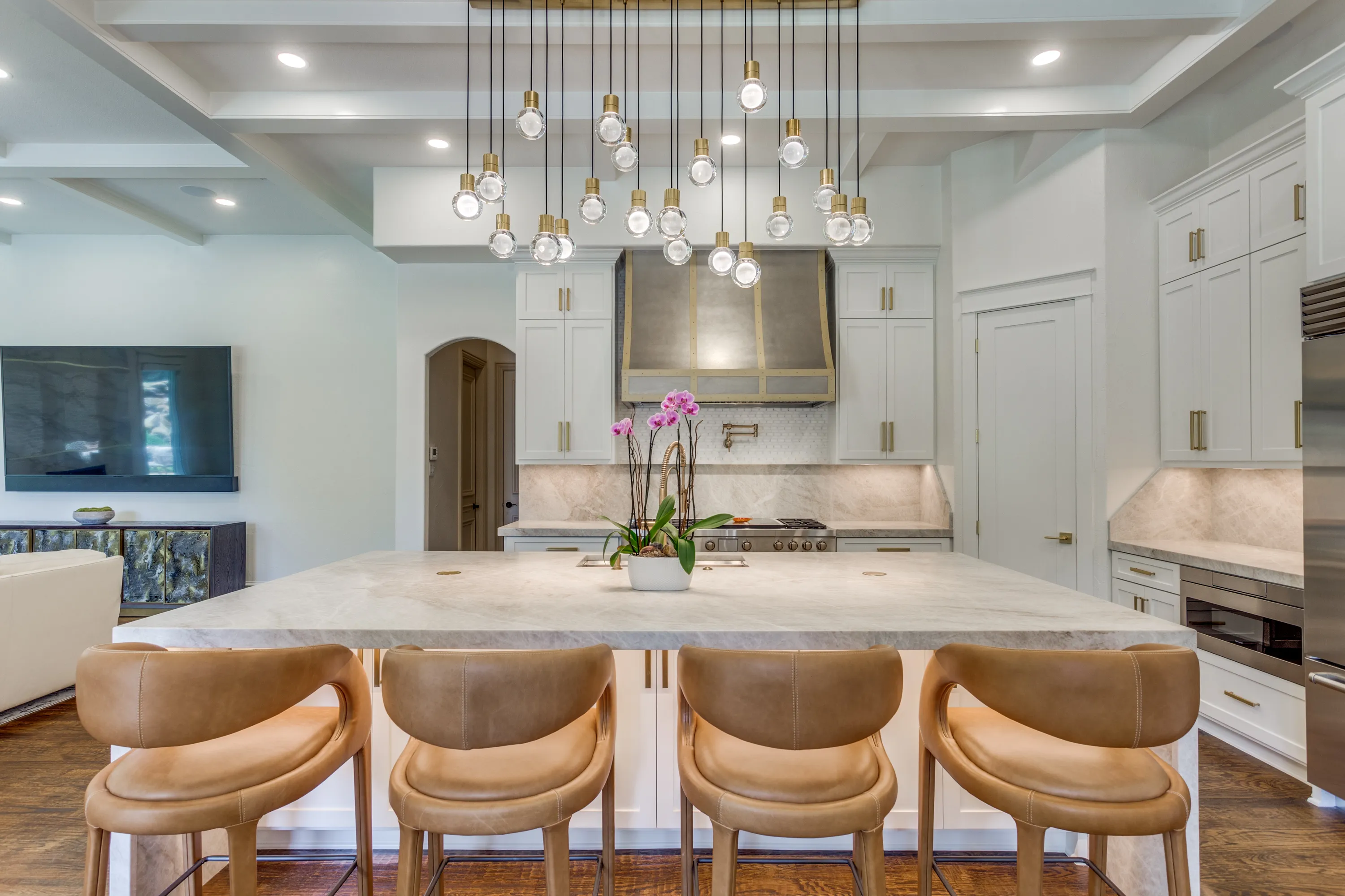 Kitchen island in Taj Mahal quartzite beneath the 21-light Visual Comfort pendant, facing the custom brass-banded range hood