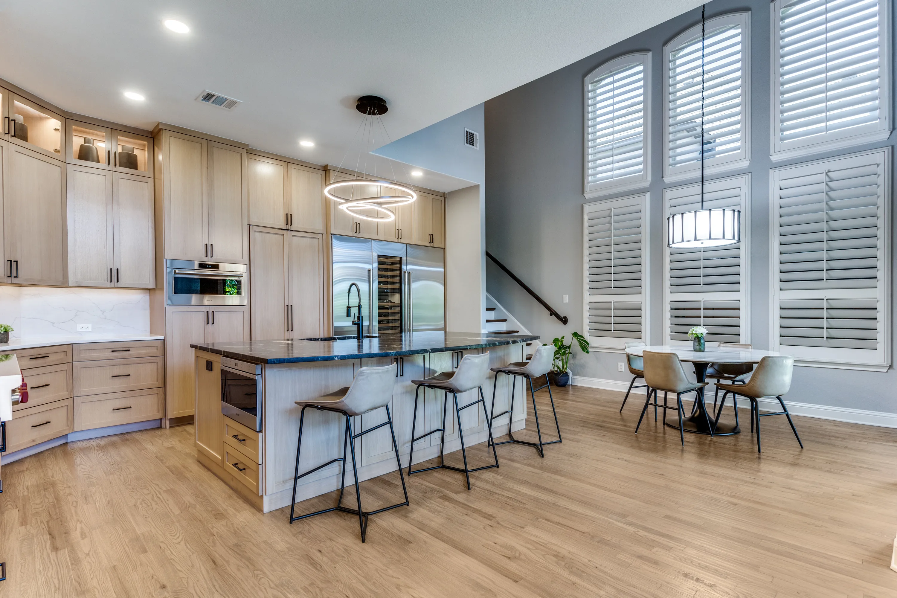 Kitchen island and breakfast nook with two-story shuttered windows and staircase beyond