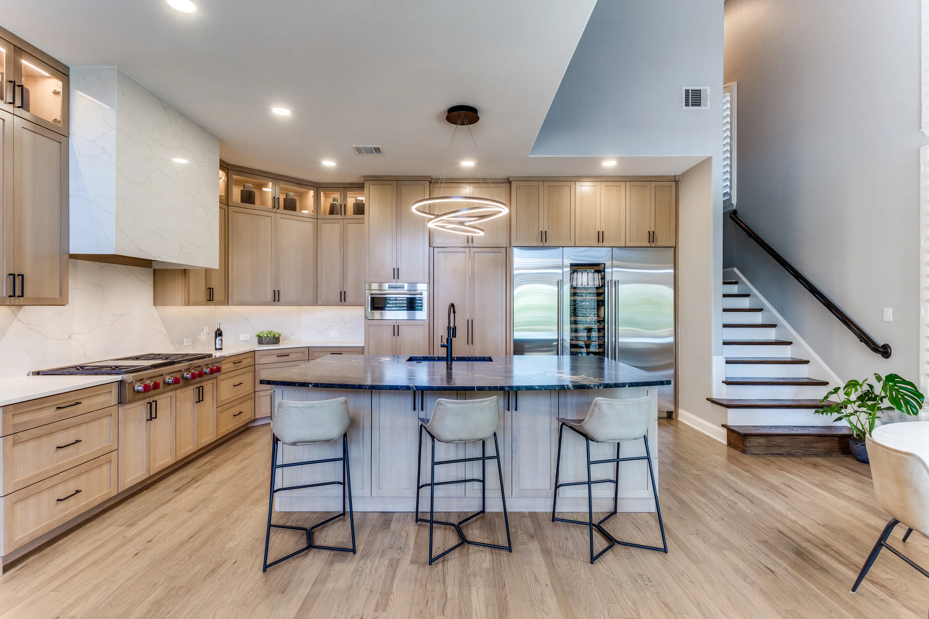 Kitchen with Belvedere granite island, sculptural ring pendant, and staircase beyond