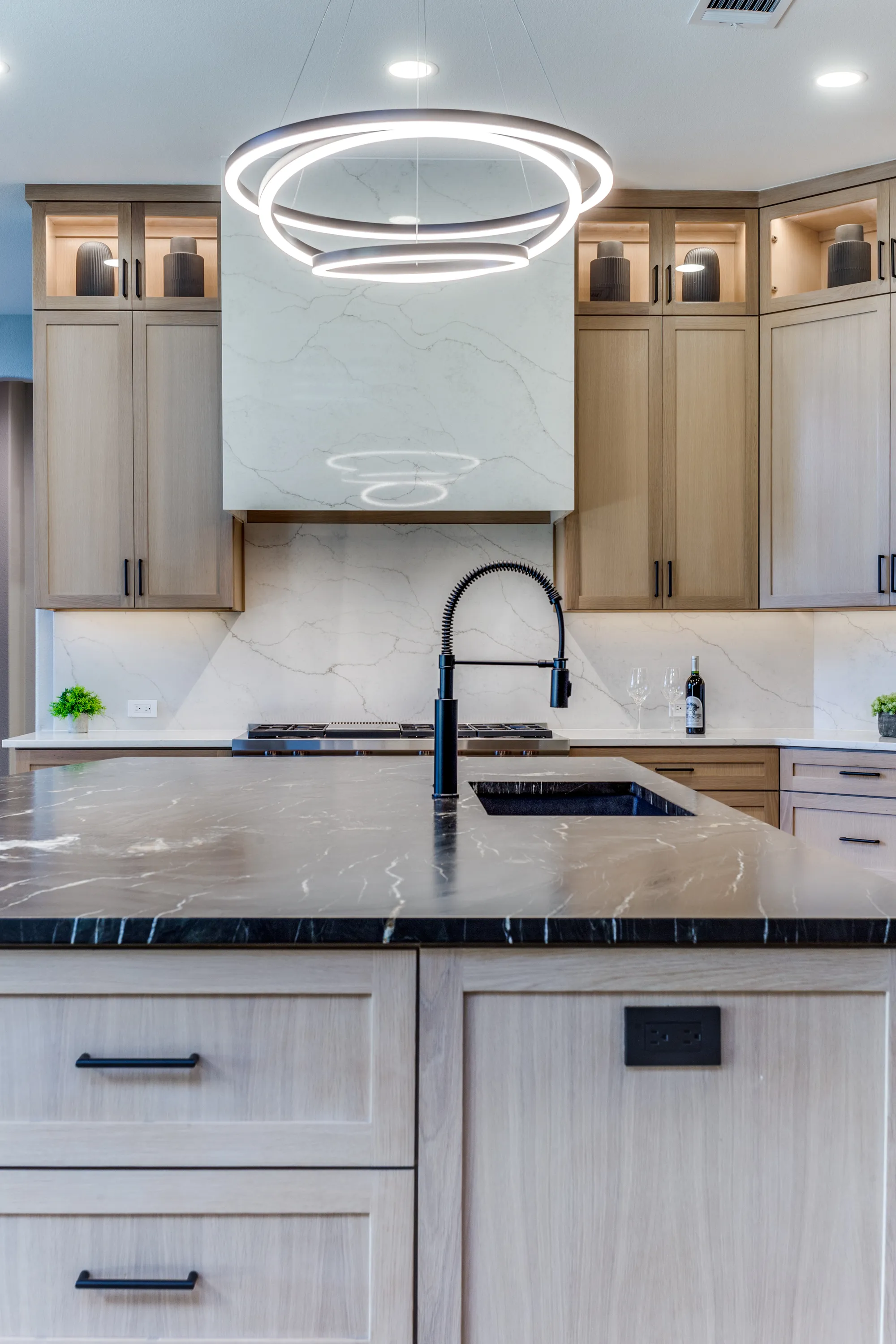 Kitchen island close-up with matte black faucet beneath the sculptural ring pendant