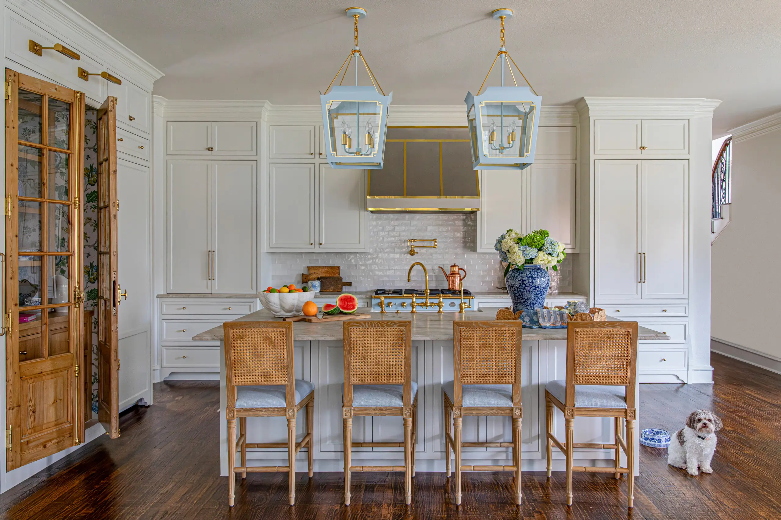 A French country kitchen with powder-blue and brass lantern pendants, a matching range, and cane-back barstools.