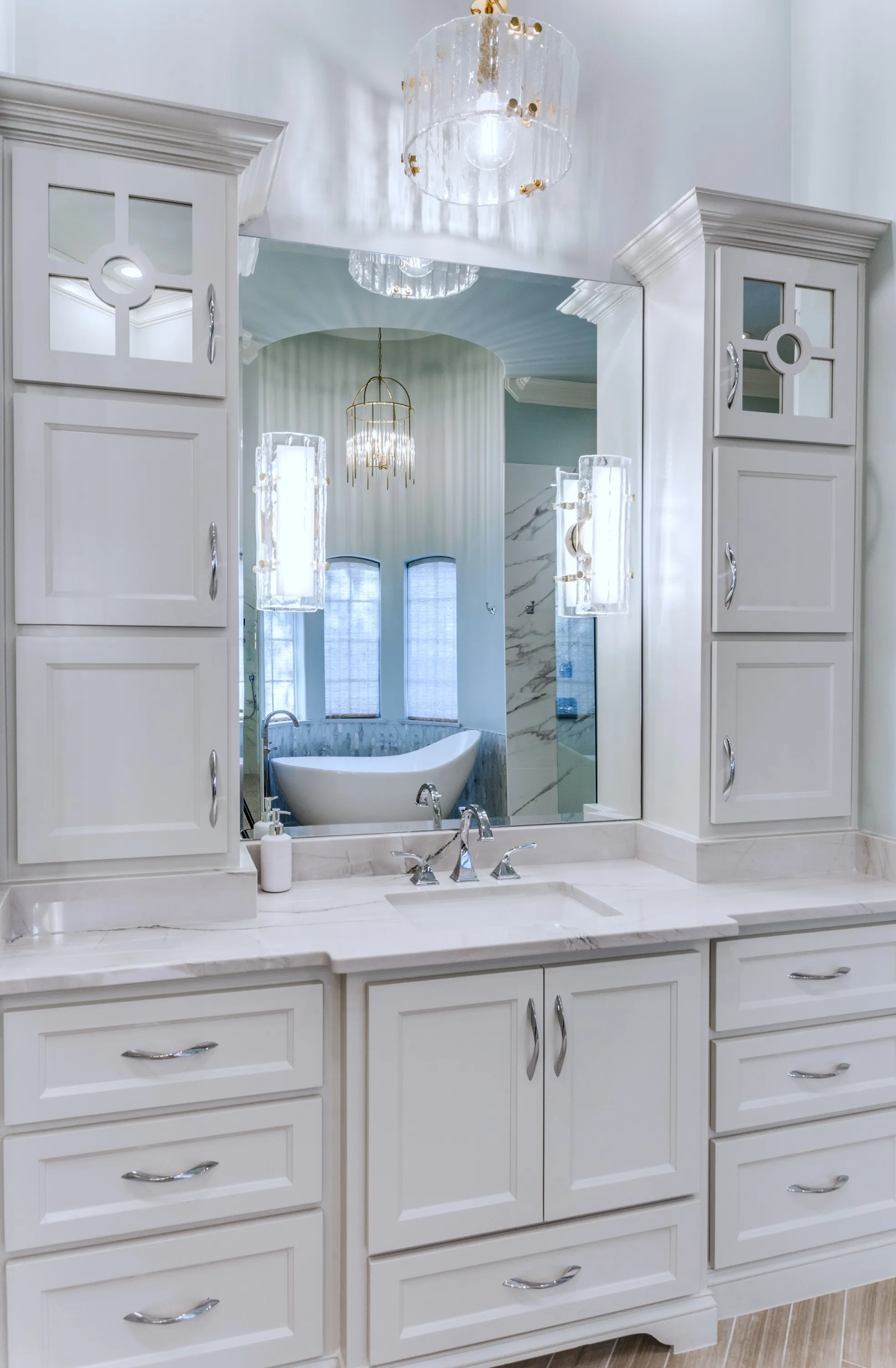 Single vanity beneath a crystal pendant, with the freestanding soaking tub and shower visible in the mirror's reflection