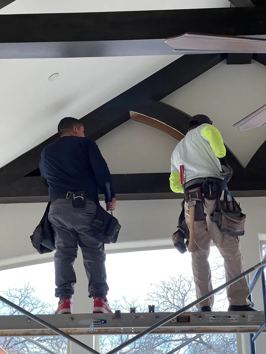 Two members of the Swanson crew on scaffold finishing a black beam with tool belts and headlamps.