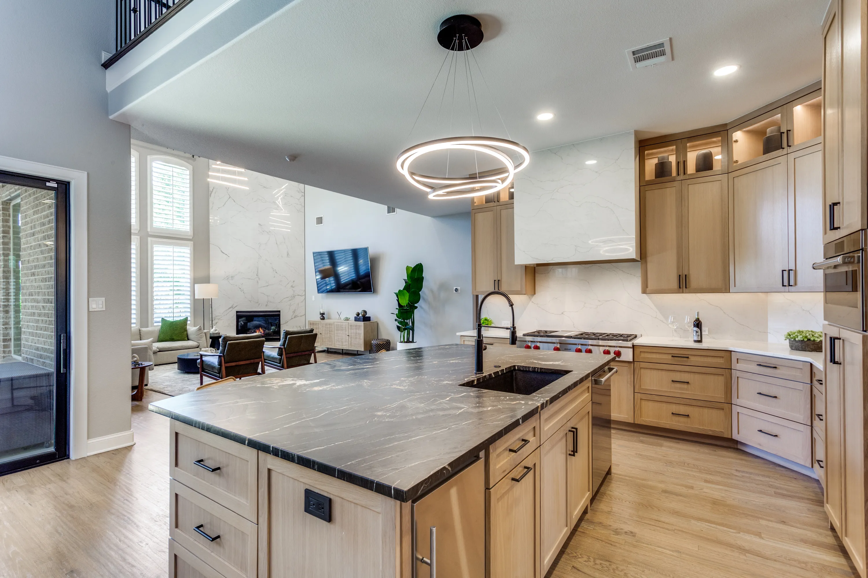 An open kitchen with a Belvedere granite island and rift-cut white oak cabinetry, opening to a two-story family room.