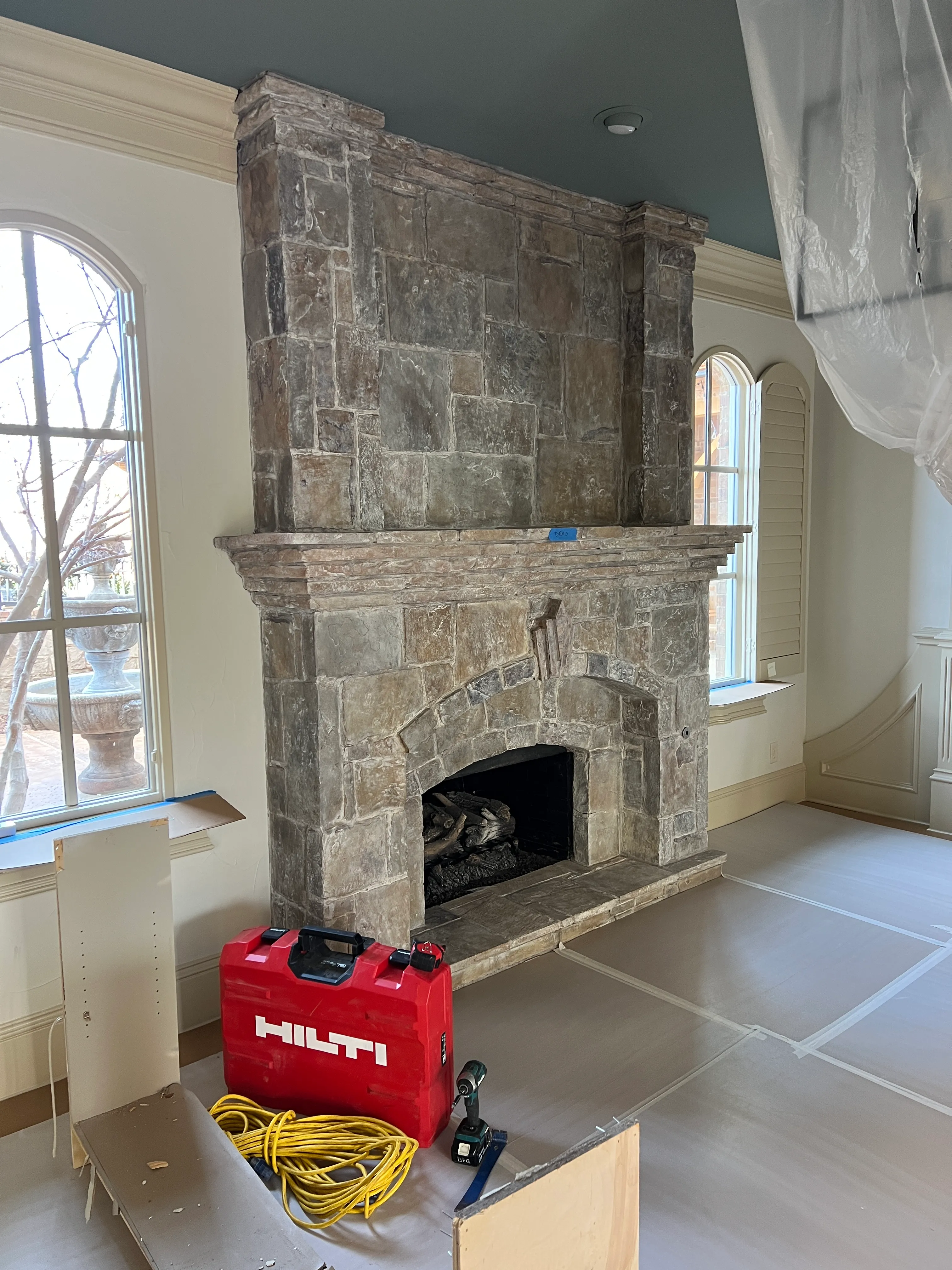 A stone chimney breast wrapped in plastic protection while adjacent trades work — Swanson's finished-area barrier standard.